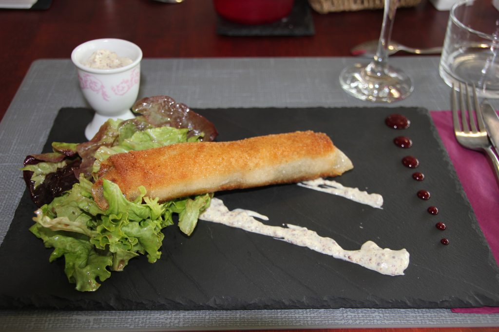 un nem farci de boudin avec une sauce moutarde, présenté sur une assiette noire