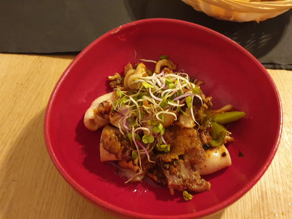 dans une assiette rouge chipirons sautés au pied de cochon et cèpes